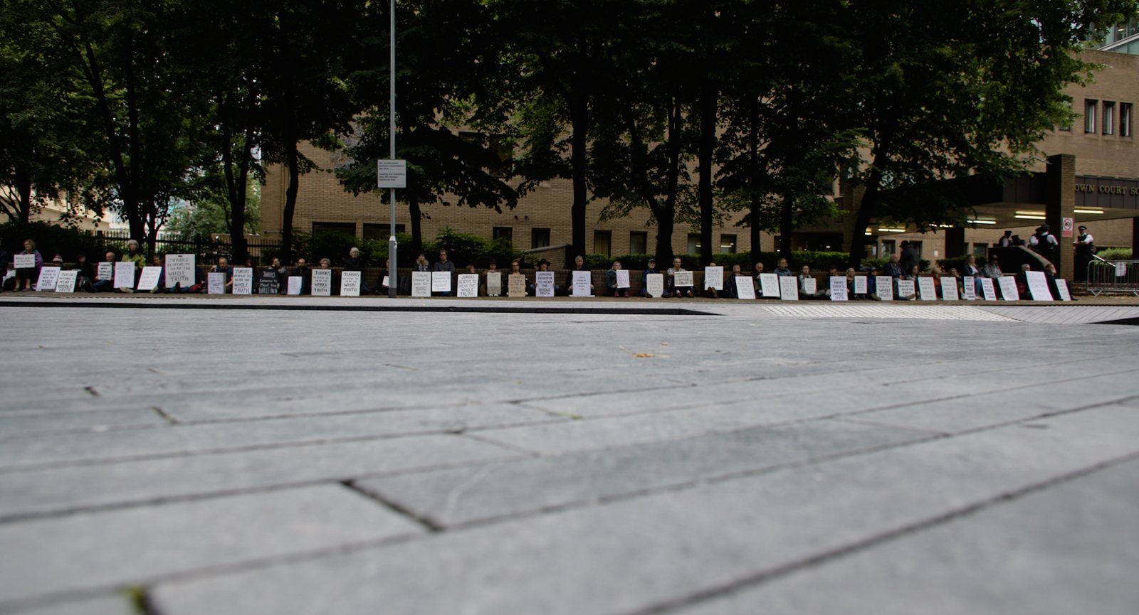 A line of people sit outside a Crown Court holding &lsquo;Jurors deserve to hear the whole truth&rsquo; signs